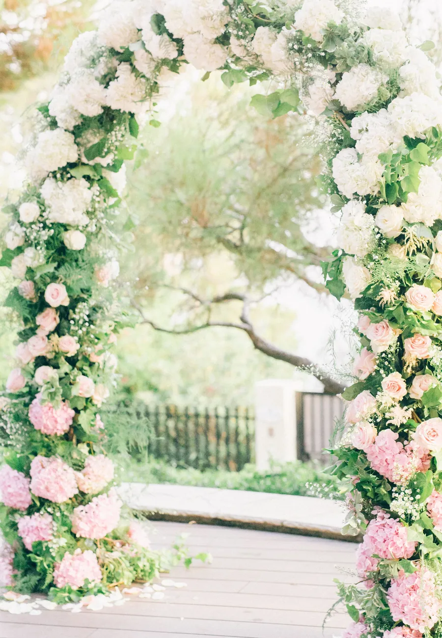 A wedding ceremony arch of white and blush roses and hydrangeas