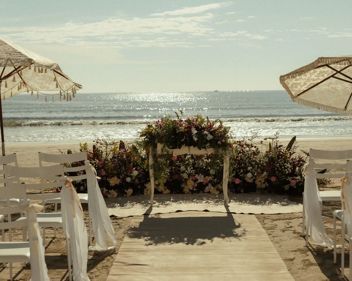 A beach wedding ceremony: aisle runner, draped chairs and a floral altar facing the ocean