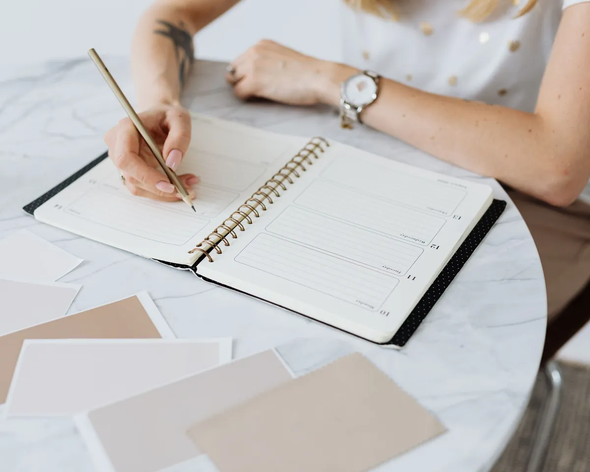 A wedding planner writing in a planning notebook beside blush stationery swatches